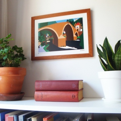 Quadro com ilustração de ponte e plantas em vasos sobre prateleira com livros