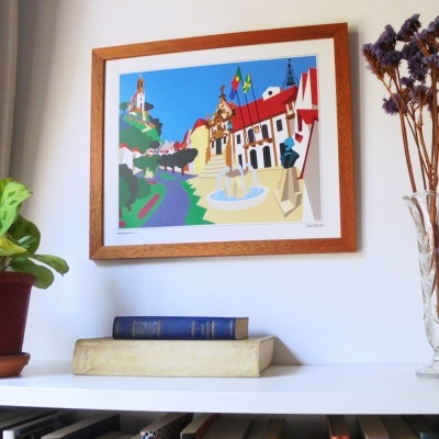 quadro emoldurado com ilustração colorida de praça com fontes, árvores e edifícios pendurado na parede
