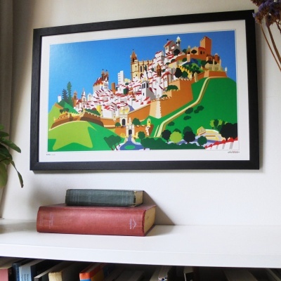 Quadro colorido de paisagem urbana pendurado numa parede, com livros sobre prateleira branca