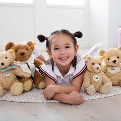 Menina deitada rodeada por ursinhos de pelúcia em quarto claro.