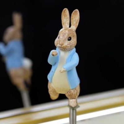 Figura decorativa de coelho com colete azul e corpo castanho claro em mola