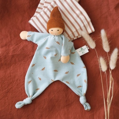 Boneco de pano com roupa azul e gorro castanho em tecido laranja com pano riscado ao fundo