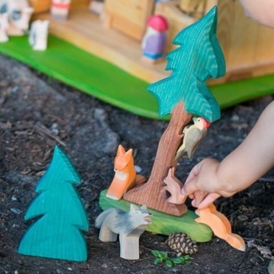 Brinquedos de madeira de animais e árvores com uma criança a brincar no chão