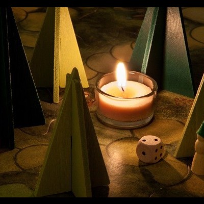 Figuras de madeira pintadas de verde, amarelo e preto, vela acesa em copo de vidro e dado branco com pontos pretos sobre superfície com padrão irregular