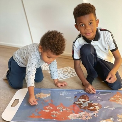 Dois meninos a jogar com um tabuleiro de jogo com mapas coloridos no chão
