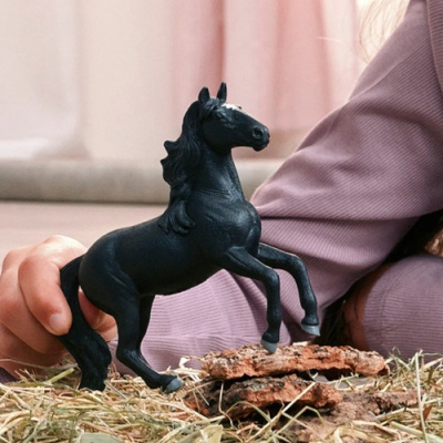Figura de cavalo preto de plástico sobre palha e madeira com mão ao fundo