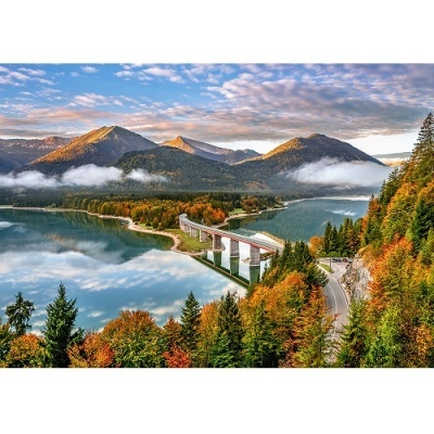Ponte em betão sobre lago com floresta e montanhas ao fundo