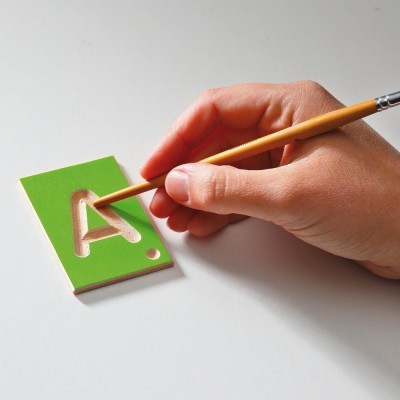 Mão pintando a letra 'A' num molde verde sobre fundo branco.