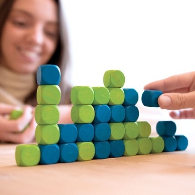 Cubos de madeira verdes e azuis empilhados em pirâmide com duas pessoas interagindo