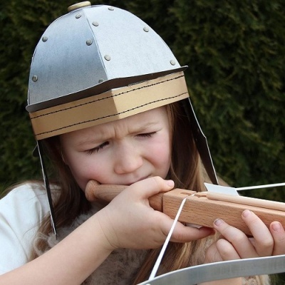 Criança com capacete prateado e besta de madeira ao ar livre