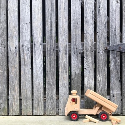 Caminhão de brinquedo de madeira com rodas vermelhas junto a cerca de madeira