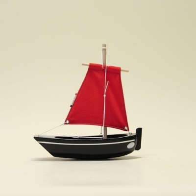 Barco de brinquedo preto com vela vermelha em fundo claro