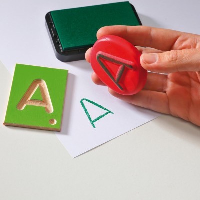 Carimbo vermelho com letra A, placa verde e tinteiro numa mesa branca