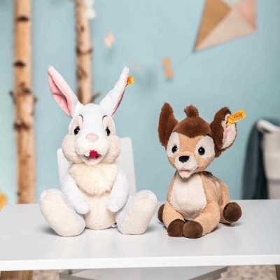 Dois peluches, um coelho branco e um cervo castanho, sentados numa mesa branca em ambiente infantil.