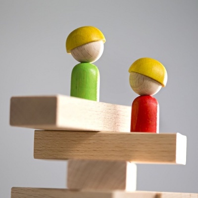 Bonecos de madeira coloridos com capacetes amarelos em blocos de madeira empilhados