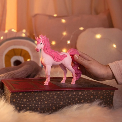 Boneco de unicórnio rosa sobre livro com capa estrelada em ambiente acolhedor