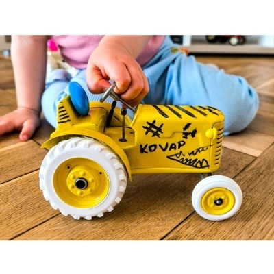 Trator de brinquedo amarelo metálico com pneus brancos no chão de madeira