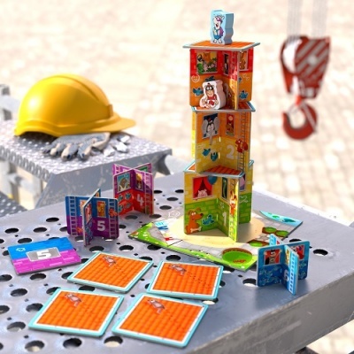 Jogo de cartas infantil colorido montado em torre ao lado de capacete amarelo numa superfície metálica.