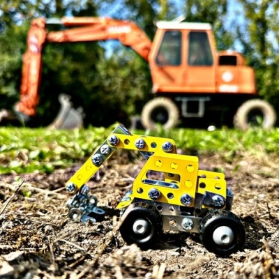 Modelo de escavadora metálica amarela e cinzenta em primeiro plano, escavadora laranja ao fundo