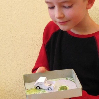 Criança a segurar caixa com modelo de carro de papel e cenário de estrada desenhado