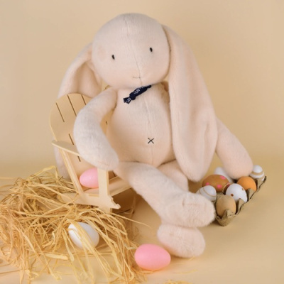 Coelho de peluche branco com cachecol azul sentado numa cadeira de madeira com ovos coloridos e palha