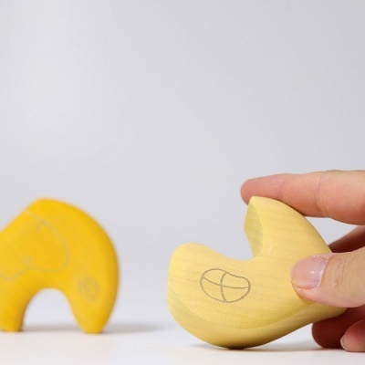 Brinquedos de madeira amarelos com padrões circulares, uma mão segura um deles