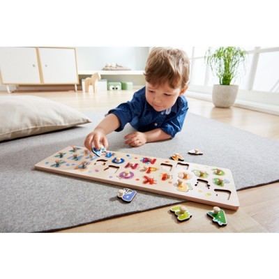 Tabuleiro de madeira com letras coloridas e menino a brincar num tapete cinzento