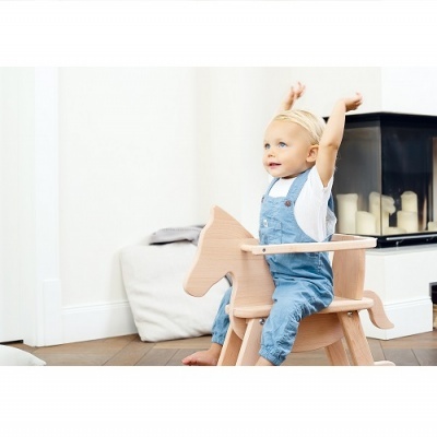 Criança em cadeira de baloiço de madeira em forma de cavalo num interior com lareira