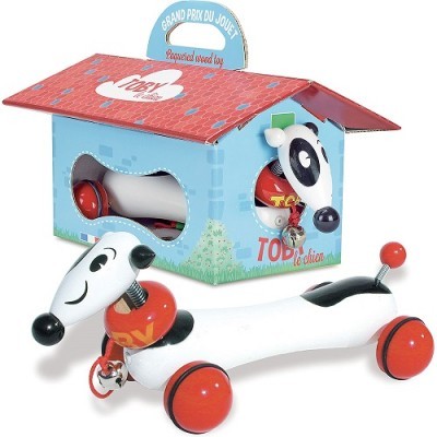 Brinquedo de cão com rodas vermelhas ao lado de casinha de papelão azul com telhado vermelho