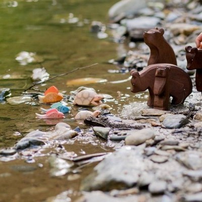 Brinquedos de madeira de ursos e peixes junto a um rio com pedras