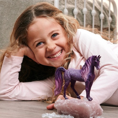 Cavalo de brinquedo roxo sobre rocha rosa com criança sorridente ao fundo
