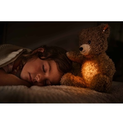 Urso de peluche iluminado ao lado de criança adormecida na cama
