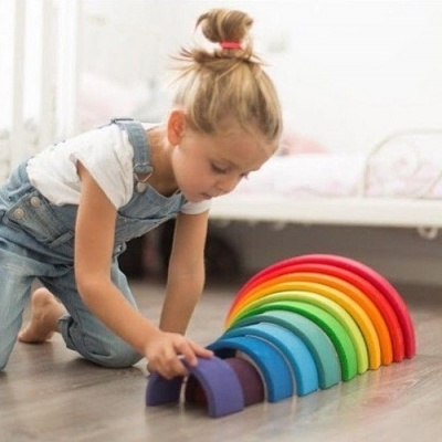 Menina brinca com arco-íris de madeira colorido num quarto
