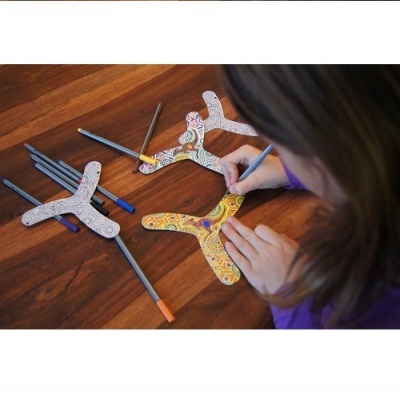 Pessoa a colorir bumerangues em madeira com canetas coloridas, mesa de madeira