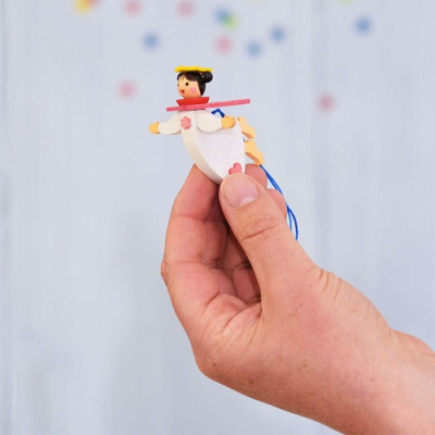 Anjo decorativo de madeira com elástico azul, em fundo claro desfocado.