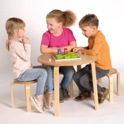 Três crianças a jogar num tabuleiro verde numa mesa redonda de madeira clara