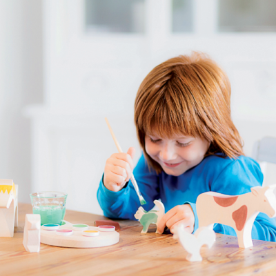 Criança a pintar figuras de animais em madeira com tintas coloridas