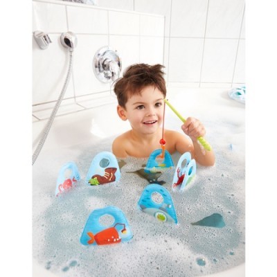 Menino a brincar com brinquedos de pesca numa banheira cheia de espuma