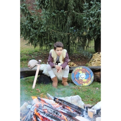 Criança com espada e escudo sentada junto a fogo ao ar livre