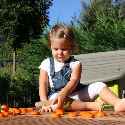 Criança a brincar com brinquedos em forma de cenoura na madeira, ao ar livre