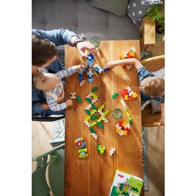 Adulto e crianças a montar brinquedo de peças de encaixar coloridas numa mesa de madeira.