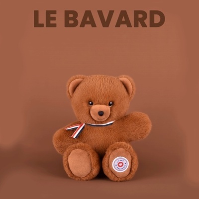Urso de peluche castanho com fita tricolor e etiqueta redonda em fundo castanho com texto LE BAVARD.