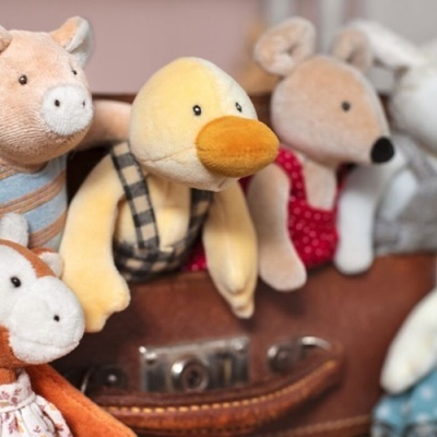 Peluches de animais coloridos com roupas, apoiados numa mala de couro castanha