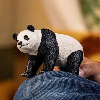 Figura pequena de panda preto e branco sobre tecido azul sendo segurada por uma mão