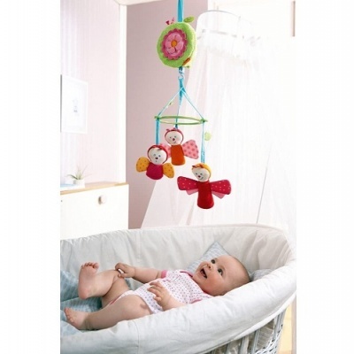 Móbile colorido com três personagens pendurados acima de um berço branco com bebé.