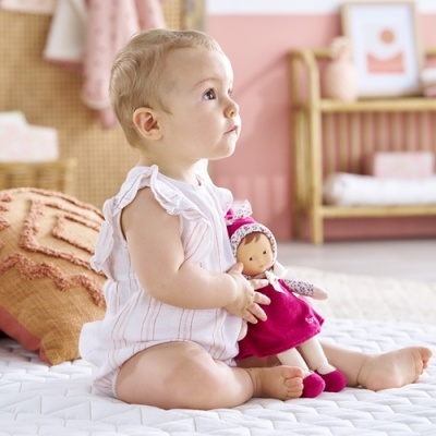 Bebé sentado segurando boneca de pano em quarto decorado com tons de rosa