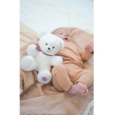 Urso de peluche branco com laço e bebé vestido de bege deitado sobre manta bege