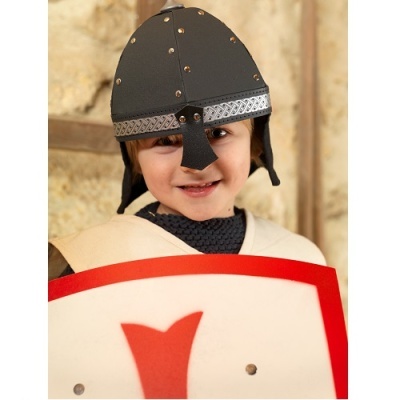 Criança com capacete preto e escudo branco e vermelho diante de parede de pedra