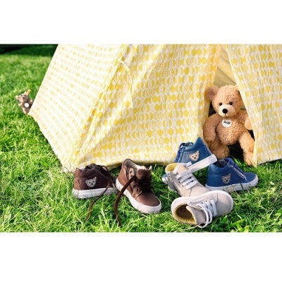 Tenda amarela, sapatilhas infantis marron, bege e azuis, urso de peluche castanho na relva