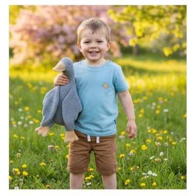 Criança sorridente com t-shirt azul e calções castanhos a segurar peluche de pato cinzento no campo